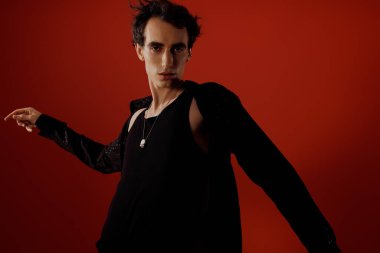 Sivri giyinmiş şık bir adam, koyu kırmızı arka planda göze çarpar..