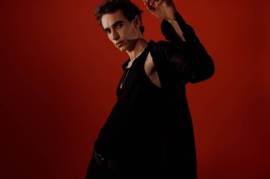 Şık bir adam kendine güvenerek kırmızı bir arka plana karşı poz veriyor, modasını gösteriyor..