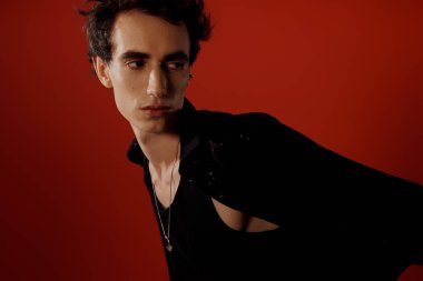 Şık bir adam, canlı kırmızı bir ortamda dengeli bir ifadeyle zarafet sergiler..