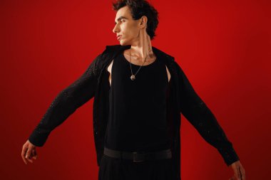 Yakışıklı bir adam şık kıyafetini sergiliyor, çarpıcı kırmızı bir arka plana karşı kendine güvenini sergiliyor..