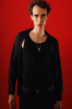 Şık giyinmiş yakışıklı adam, kendine güvenerek kırmızı bir zemine karşı duruyor ve tarzını vurguluyor..