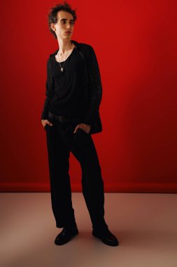 Zarif giyinmiş kendine güvenen bir adam cesur, kırmızı bir arka plana karşı duruyor..