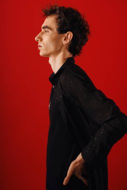 Zarif giyinmiş yakışıklı bir adam canlı kırmızı bir arka planda kendine güvenen bir yan profil çizer..