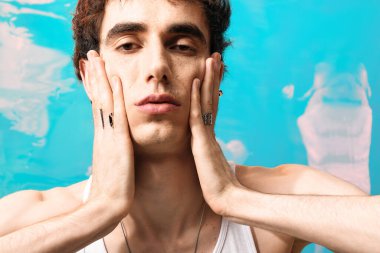 Zarif giyinmiş yakışıklı bir adam turkuaz suda sakin bir ifadeyle şık poz verir..