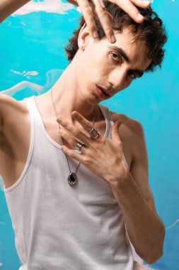 Şık giyinmiş yakışıklı bir adam parlak mavi bir arkaplanda şakacı bir şekilde poz veriyor..