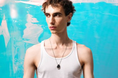 Zarif giyinmiş şık bir adam canlı mavi bir arkaplan önünde duruyor..