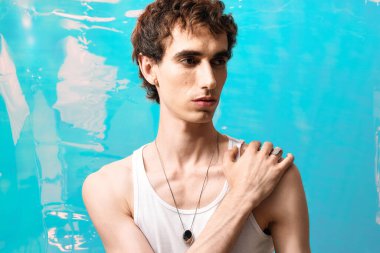 Zarif bir adam modern zarafeti sergilerken parlak mavi önünde güvenle poz verir..