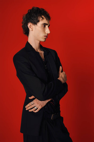 Одетый в сложную одежду, красивый мужчина уверенно позирует со скрещенными руками.