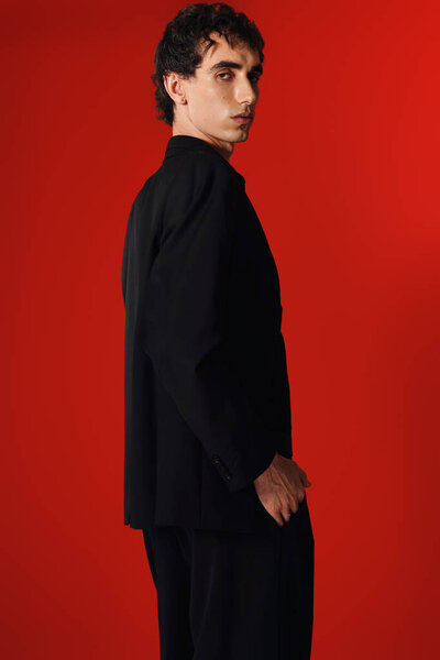 Стильный мужчина в элегантной одежде уверенно позирует, подчеркивая современную моду против яркого цвета.