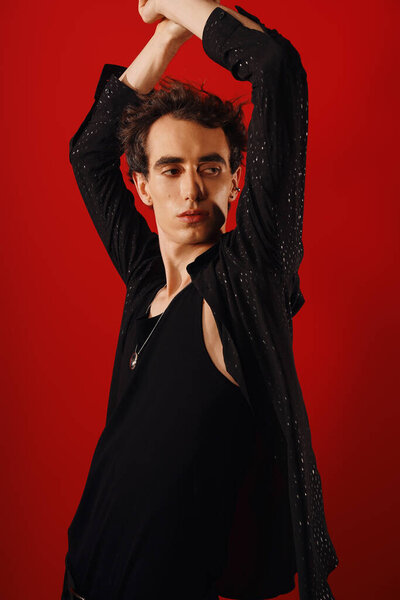 Элегантный мужчина уверенно позирует, демонстрируя свое чувство стиля на ярком красном фоне.