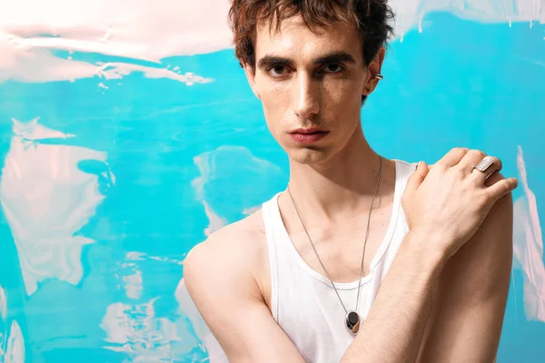 Zarif giyinmiş şık bir adam çarpıcı bir mavi arka plana karşı duruyor..