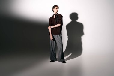 Handsome young man poses in chic outfit, casting an intriguing shadow on the wall.