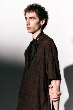 A handsome young man poses confidently in a stylish outfit within a minimalist space.