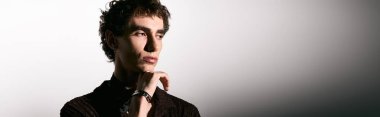 An elegant young man poses thoughtfully, showcasing his fashion sense and charm in modern attire.