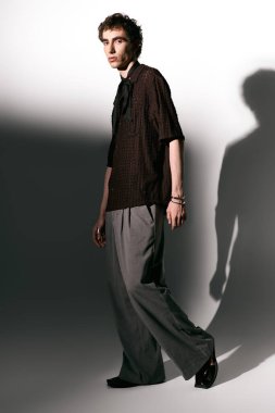 Handsome young man showcases modern fashion with a confident stance against a simple backdrop.