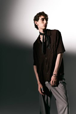 A young man stands confidently in sleek fashion, wearing trendy clothing with striking accessories.