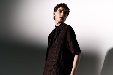 Handsome young man stands confidently in a stylish outfit against a simple backdrop.