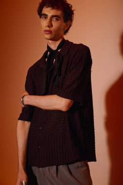 A young man with a confident expression displays fashionable attire against a warm backdrop.