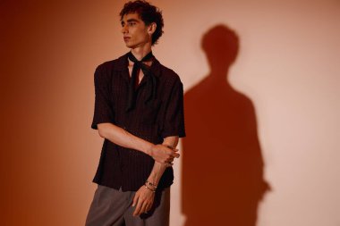 Handsome young man stands poised in chic attire against a warm, artistic backdrop.