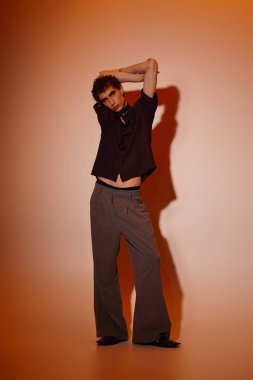 Confident young man in trendy attire shines under a soft orange glow, showcasing his style.