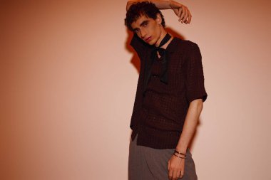 Handsome young man poses confidently in fashionable attire against a striking backdrop.