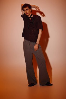 A young man stands confidently in trendy attire, expressing modern style against a warm backdrop.