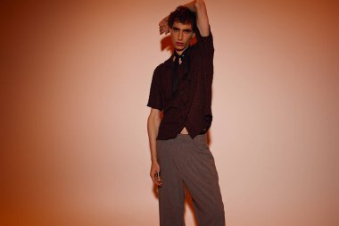 A confident young man poses in stylish clothing against a warm backdrop, exuding charm and elegance.