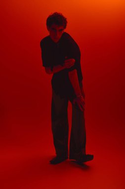 A handsome young man poses confidently in fashionable clothes with a striking orange background.