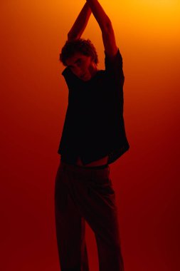 A confident young man displays his fashion sense in a vibrant setting with warm hues.