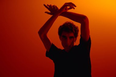 A handsome young man poses dramatically against a warm orange backdrop, showcasing his style.