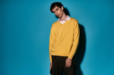 Stylish young man models a trendy yellow sweater and dark pants, exuding modern charm.