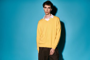 Handsome young man stands confidently, wearing a trendy yellow sweater paired with dark pants.
