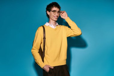 Handsome young man wears a bright yellow sweater and glasses, smiling confidently in trendy style.
