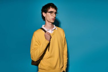 A handsome young man stands confidently, wearing a bright yellow sweater and glasses.