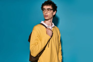 Stylish young man poses confidently with a backpack, exuding charisma.