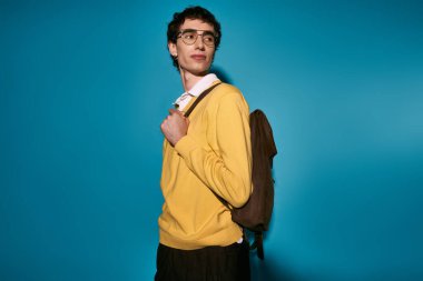 A handsome young man displays his fashion sense in a yellow sweater and glasses, smiling happily.