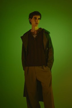 A stylish young man poses confidently against a green background.