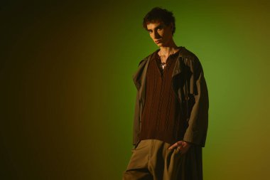 A handsome young man stands confidently, displaying his stylish attire in warm, colorful lighting.