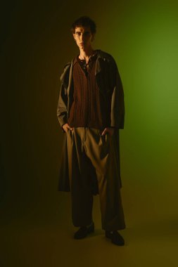 Handsome young man stands confidently in stylish attire against a vibrant green background.