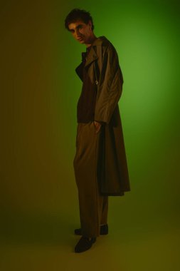 A handsome young man stands confidently in a trendy outfit, highlighted by colorful lighting.