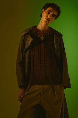 Handsome young man dressed in stylish attire stands confidently in a bright setting.