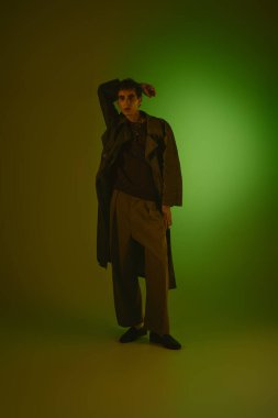 Handsome young man showcases modern fashion in a uniquely lit environment, exuding charisma.