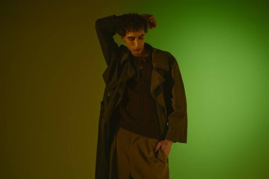 A handsome young man dressed in trendy attire poses thoughtfully in a colorful setting.