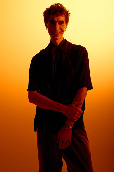 Handsome young man stands confidently with a smile, radiating style in a warm setting.