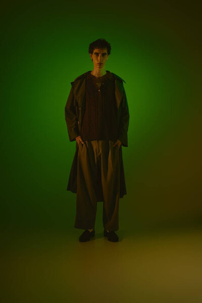 Young man stands confidently, showcasing stylish outfit in dramatic green glow.