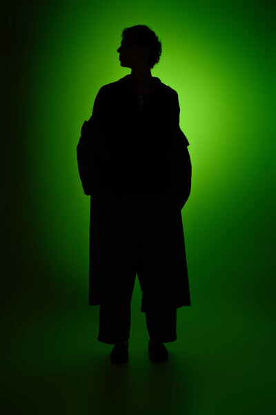 A stylish young man poses gracefully against a striking green backdrop, exuding charm.