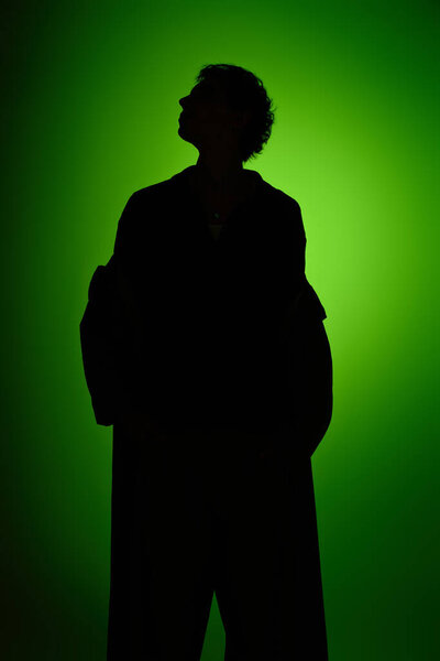 A handsome young man stands confidently, casting a striking silhouette with a bold green background.