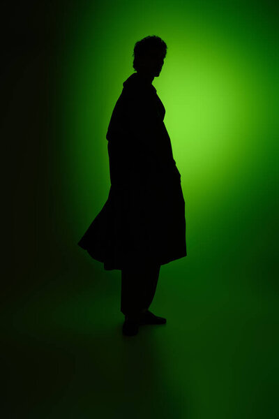 A fashionable young man strikes a pose, his silhouette highlighted by a striking green light.