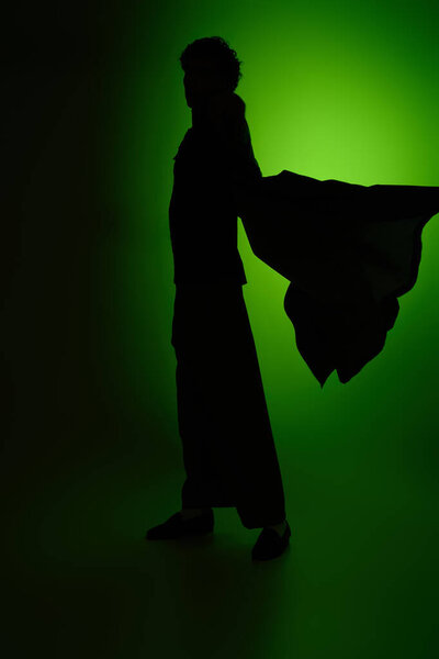 A stylish young man poses confidently against a vibrant green backdrop.