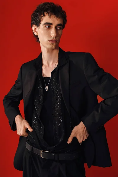 Ein fescher Mann in eleganter Kleidung steht selbstbewusst da und strahlt Stil vor leuchtend rotem Hintergrund aus.. — Stockfoto